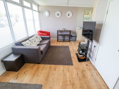 A living room with a gray sofa red chair wall art and a mounted television at 68 Cherry Park in Chapel St Leonards