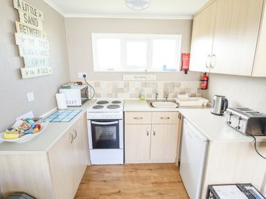 A small kitchen with stove microwave kettle toaster and sink at 68 Cherry Park in Chapel St Leonards