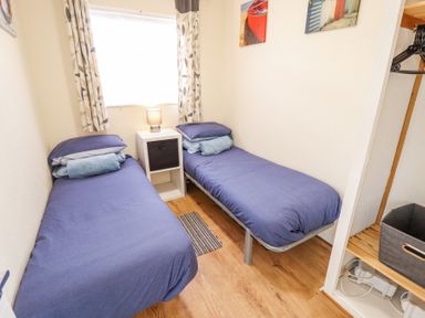 A bedroom with two single beds a small table with a lamp between the beds and an open closet at 68 Cherry Park in Chapel St Leonards