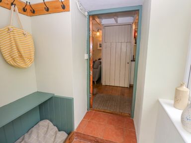 A hallway with a wooden bench and hooks on the wall leading to a room with a wooden door and a rug on the floor at 2 Summerhill in Letterston