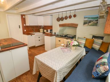 A kitchen with a wooden floor and white cabinets a table with a polka dot tablecloth and a bench with cushions at 2 Summerhill in Letterston