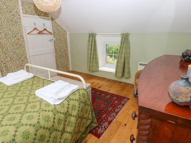 A small bedroom with a bed, wooden floor, patterned wallpaper, a window with curtains and a wooden dresser at 2 Summerhill Letterston