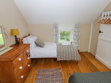 A bedroom with a single bed dresser with a lamp and mirror and window with curtains at 2 Summerhill in Letterston