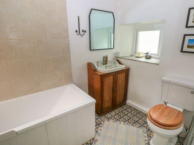 A bathroom with a bathtub wooden sink cabinet toilet with wooden seat and patterned floor at 2 Summerhill in Letterston