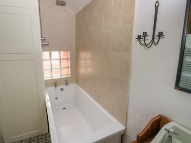 A bathroom with a bathtub shower combination tiled walls a glass block window candle holder faucet and a mirror at 2 Summerhill in Letterston