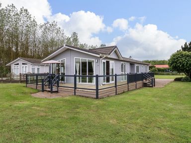 A grey wooden lodge with large windows and a fenced wooden deck on a grassy area at Owls Retreat Lodge 11 Near Aldeburgh