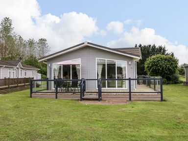 A wooden lodge with a deck and outdoor table with umbrella on a grassy area at Owls Retreat Lodge 11 Near Aldeburgh