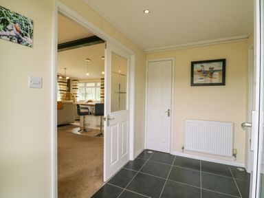 A hallway with tiled floor white doors and a radiator leading to a living room with chairs and curtains at Owls Retreat Lodge 11 Near Aldeburgh