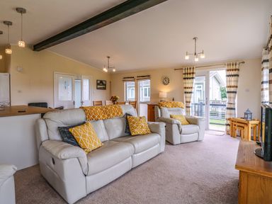 A living room with leather sofas yellow cushions dining table and kitchen area at Owls Retreat Lodge 11 Near Aldeburgh