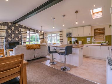 An open plan kitchen and living area with bar stools dining table sofa and large windows at Owls Retreat Lodge 11 Near Aldeburgh