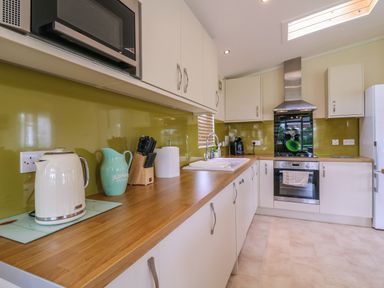 A kitchen with white cabinets wooden countertops a kettle a knife block and a stove at Owls Retreat Lodge 11 Near Aldeburgh