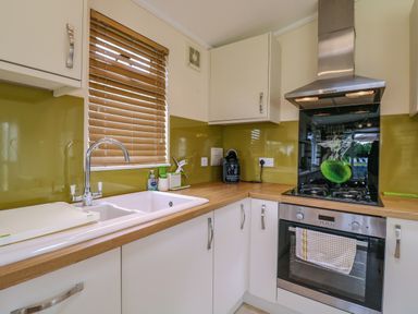 A kitchen with a sink, countertop, gas stove, oven, cabinets, and window blinds at Owls Retreat Lodge 11 Near Aldeburgh