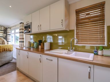 A kitchen with white cabinets a wooden countertop a sink a window with blinds and kitchen utensils at Owls Retreat Lodge 11 Near Aldeburgh