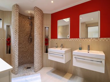 A bathroom with a curved tiled shower, two wall-mounted sinks with mirrors and a red accent wall at Owls Retreat Lodge 11 Near Aldeburgh