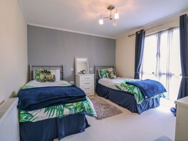 A bedroom with two single beds with leaf print bedding and blue throws at Owls Retreat Lodge 11 Near Aldeburgh