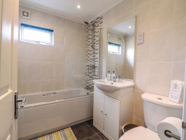 A bathroom with a bathtub shower combo a sink with a cabinet a toilet and a window at Owls Retreat Lodge 11 Near Aldeburgh