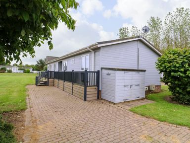 A single story house with a small storage shed and a fenced patio area on a paved driveway at Owls Retreat Lodge 11 Near Aldeburgh