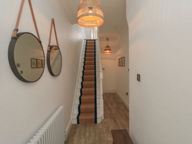 A narrow hallway with wooden flooring and stairs with a carpet runner in the center and two round mirrors hanging on the left wall at Thirty Four By the Sea in Scarborough