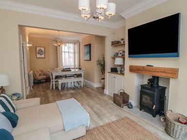 A living room with a wood-burning stove and a TV mounted above it next to a dining area with a white table and chairs at Thirty Four By the Sea in Scarborough