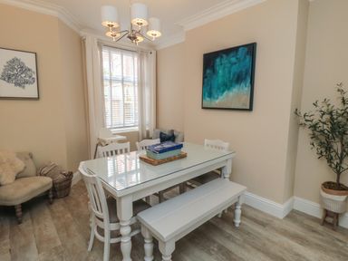 A dining room with a white table and chairs a bench a window with curtains and a plant in a pot at Thirty Four By the Sea in Scarborough