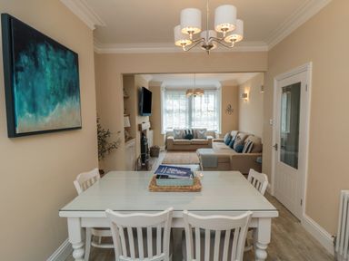 A dining area with a white table and chairs leading to a living room with sofas and a window at Thirty Four By the Sea in Scarborough