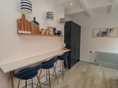 A kitchen area with a long counter and three blue bar stools under striped pendant lights at Thirty Four By the Sea in Scarborough