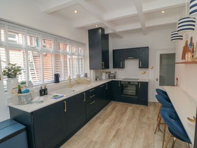 A kitchen with black cabinets white countertops a sink an oven blue chairs at a breakfast bar and windows with blinds at Thirty Four By the Sea in Scarborough