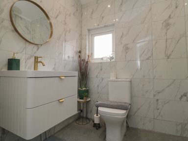 A bathroom with a toilet sink cabinet round mirror and small table with plants at Thirty Four By the Sea in Scarborough