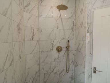 A shower area with marble patterned tiles a showerhead and a door handle at Thirty Four By the Sea in Scarborough