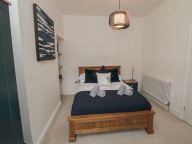 A bedroom with a wooden bed frame navy bedding rolled towels on the bed a bedside table with a lamp and a radiator on the wall at Thirty Four By the Sea in Scarborough