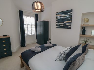 A bedroom with a bed and rolled towels pillows a wardrobe chest of drawers window and wall art at Thirty Four By the Sea in Scarborough