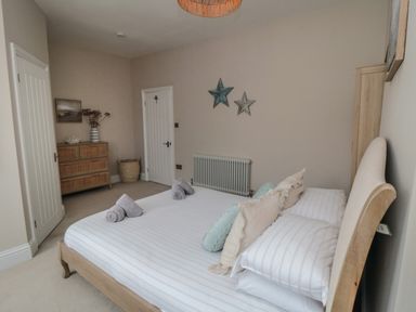 A bedroom with a bed, pillows, rolled towels, a chest of drawers, wall decorations, and two doors at Thirty Four By the Sea in Scarborough