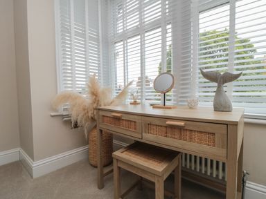A wooden dressing table with a small mirror a whale tail decoration and pampas grass in a woven basket by a window with white blinds at Thirty Four By the Sea in Scarborough