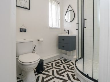 A bathroom with a toilet, floating vanity with sink, round mirror, and curved glass shower enclosure at Thirty Four By the Sea in Scarborough