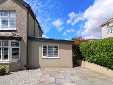 The side of a house with a paved patio area and gravel next to a hedge and shrubs at 3 Palms in Preston Sands