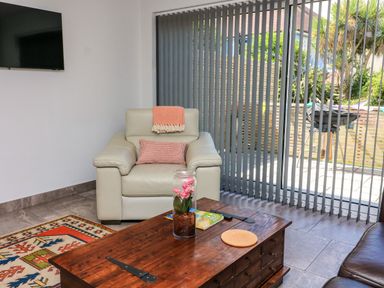 A living room with a leather armchair a wooden coffee table and vertical blinds at 3 Palms in Preston Sands