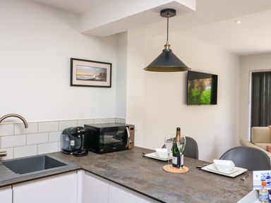 A kitchen area with a sink coffee machine microwave and a dining counter set with plates glasses and a bottle at 3 Palms in Preston Sands