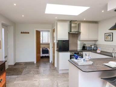 A kitchen with white cabinets a small black fridge and an open door showing a bedroom at 3 Palms in Preston Sands