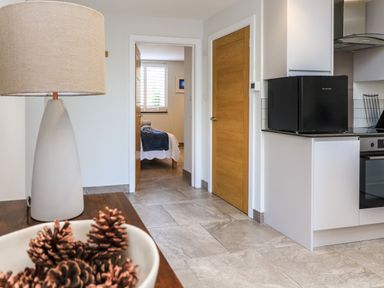 A kitchen area with a black microwave on the counter and a view into a bedroom with a bed and window at 3 Palms in Preston Sands