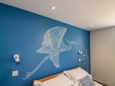 A bedroom with a wooden bed blue and white patterned pillows and a blue wall with a white bird mural at 3 Palms in Preston Sands