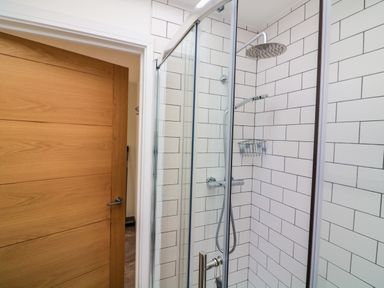 A shower area with glass door and white tiled walls and a wooden door nearby at 3 Palms in Preston Sands
