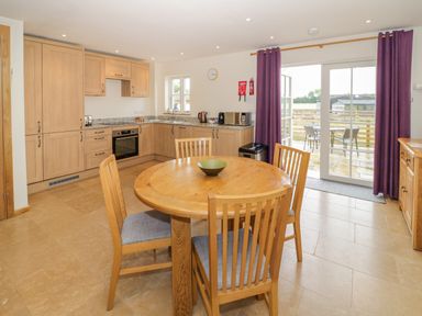 A kitchen with wooden cabinets a round wooden dining table with four chairs and purple curtains at Lavender Cottage in Oxhill near Tysoe