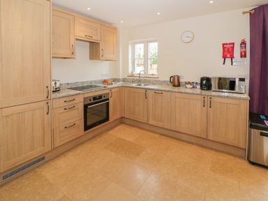 A kitchen with wooden cabinets a built-in oven a microwave kettle and toaster at Lavender Cottage in Oxhill near Tysoe