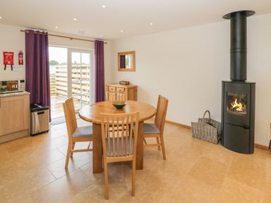 A dining area with a round wooden table and four chairs a fireplace and sliding glass doors with purple curtains at Lavender Cottage in Oxhill near Tysoe