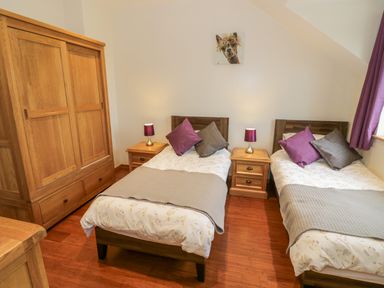 A bedroom with two single beds two bedside tables with lamps and a wooden wardrobe at Lavender Cottage in Oxhill near Tysoe