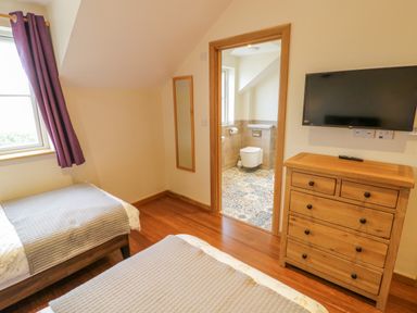 A bedroom with two single beds a wooden chest of drawers and a wall-mounted tv at Lavender Cottage in Oxhill near Tysoe