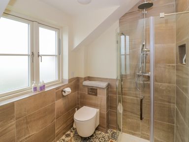 A bathroom with a window three soap bottles a toilet a towel and a glass shower enclosure at Lavender Cottage in Oxhill near Tysoe