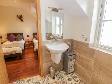 A bathroom with a sink mirror and decorative storage unit next to a bedroom with two single beds at Lavender Cottage in Oxhill near Tysoe