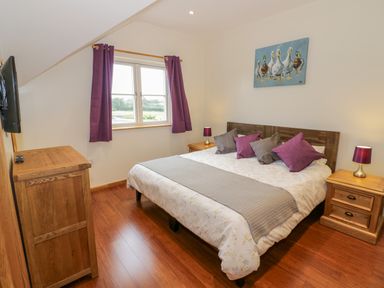 A bedroom with a double bed purple curtains and wooden furniture at Lavender Cottage in Oxhill near Tysoe