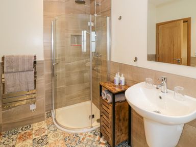 A bathroom with a glass shower enclosure a white sink and a wooden cabinet with towels at Lavender Cottage in Oxhill near Tysoe